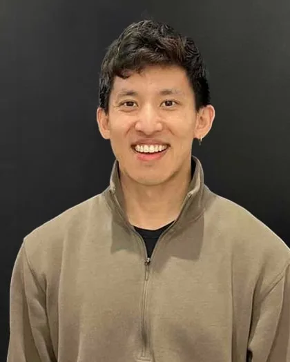 Neal Jean smiling, in an olive quarter-zip sweater against a dark wall